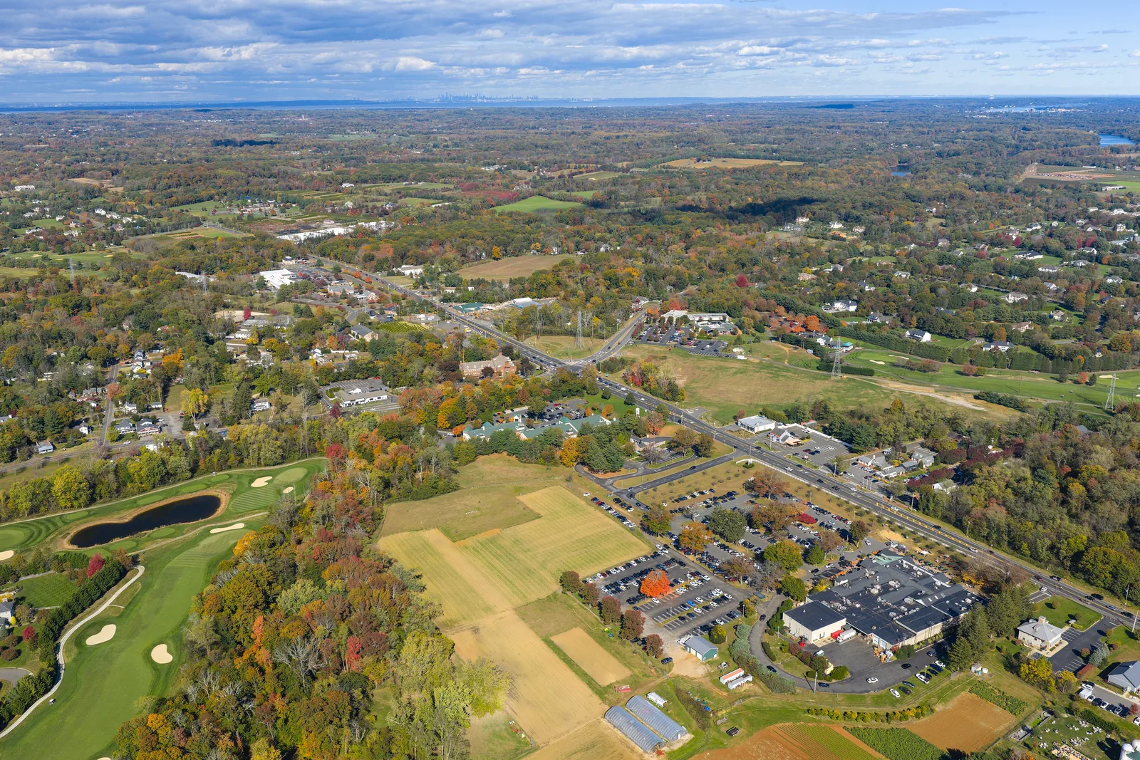 Aerial view over Colts Neck in autumn, with a golf course, farm fields and the business district along a main road among the trees