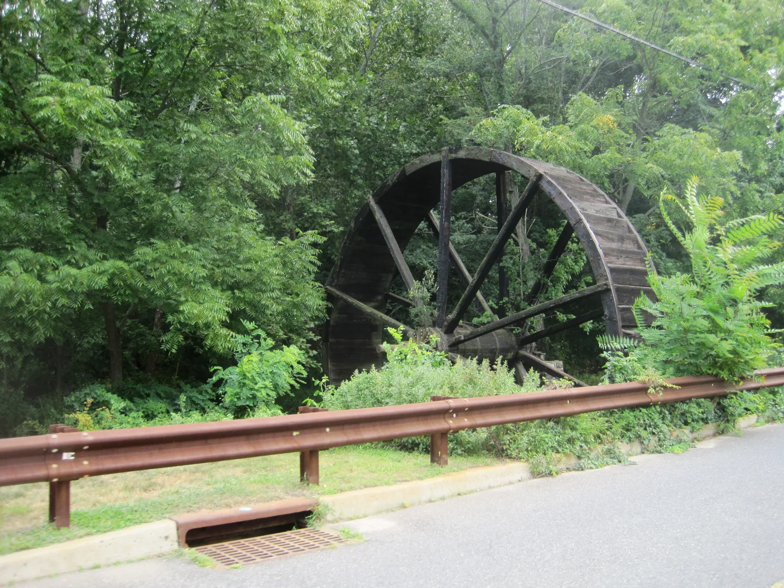 A large wooden water wheel among green trees at Bucks Mill
