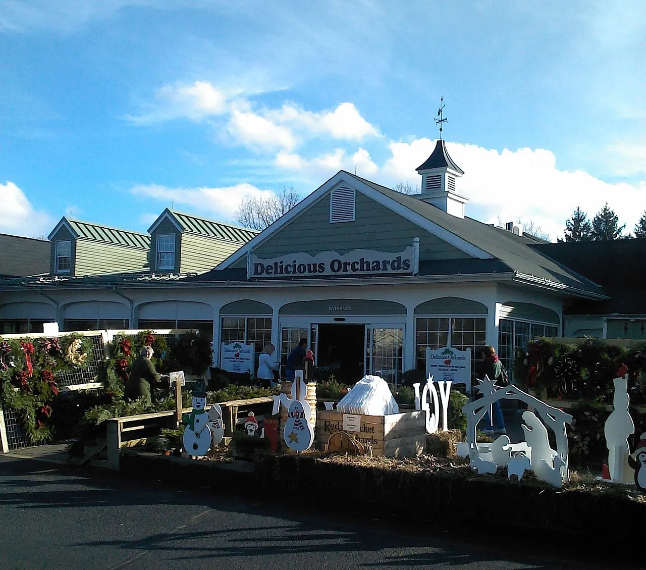 A farm market storefront with a cupola and a holiday display of wreaths and figures out front