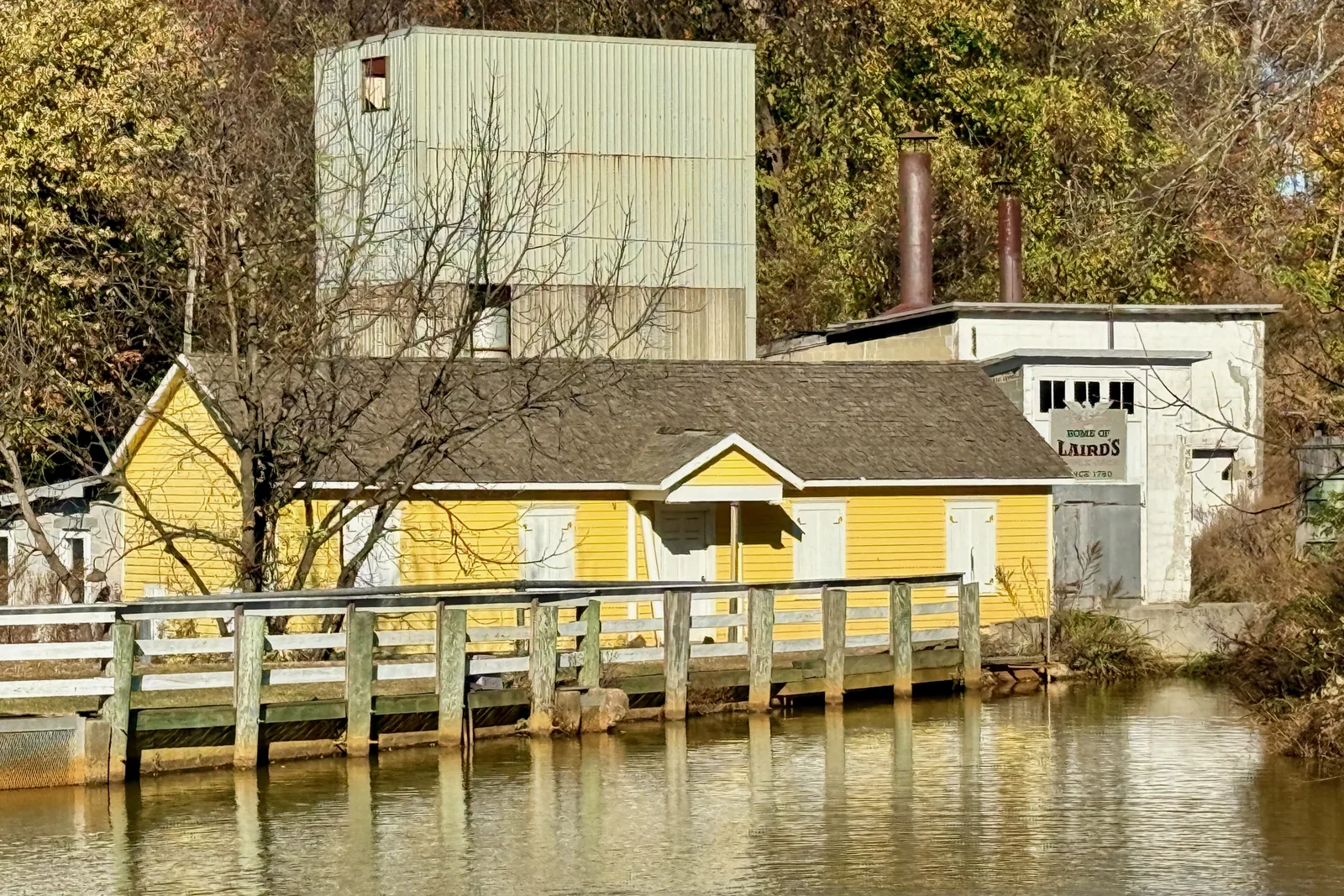 The yellow Still House of Laird and Company on a pond in Scobeyville, with autumn trees