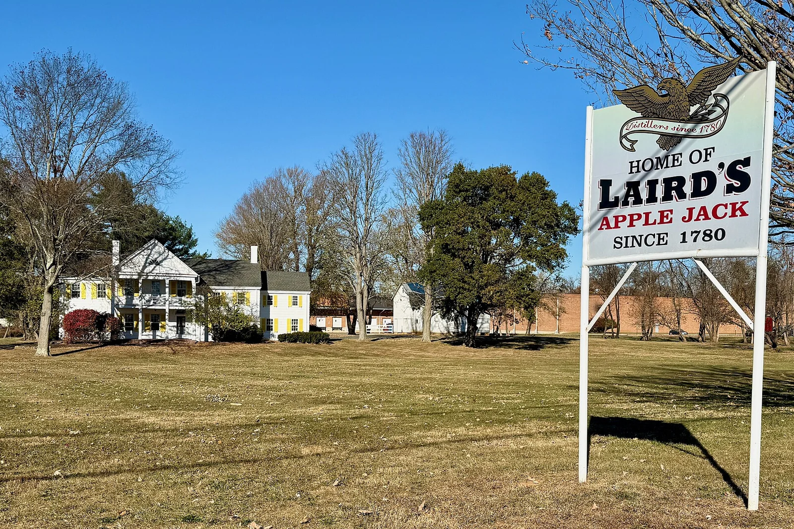 A roadside sign reading Home of Laird's Apple Jack, since 1780, in front of historic white houses in Scobeyville