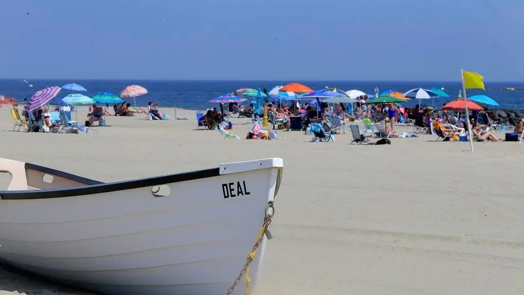 A white lifeguard boat marked DEAL on the sand in front of colorful beach umbrellas on a summer day