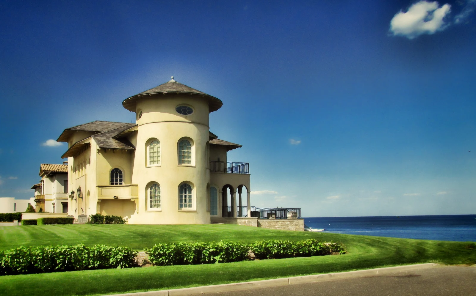 A cream-colored house with a round tower and arched windows on a green lawn beside the ocean in Deal