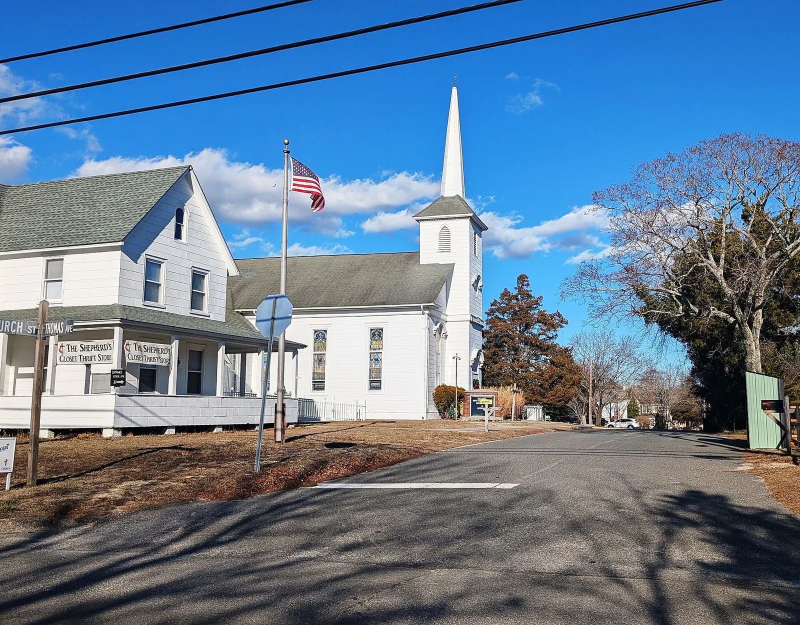 White clapboard West Creek United Methodist Church with a tall steeple and an American flag, seen from Thomas Avenue