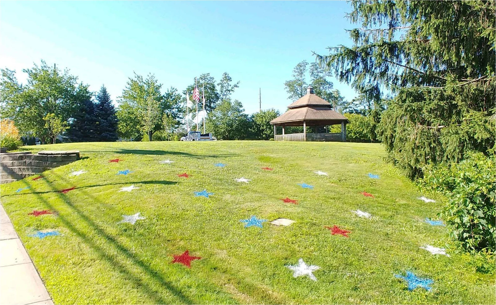 A wooden gazebo and flagpoles on a grassy hillside lawn decorated with painted red, white and blue stars