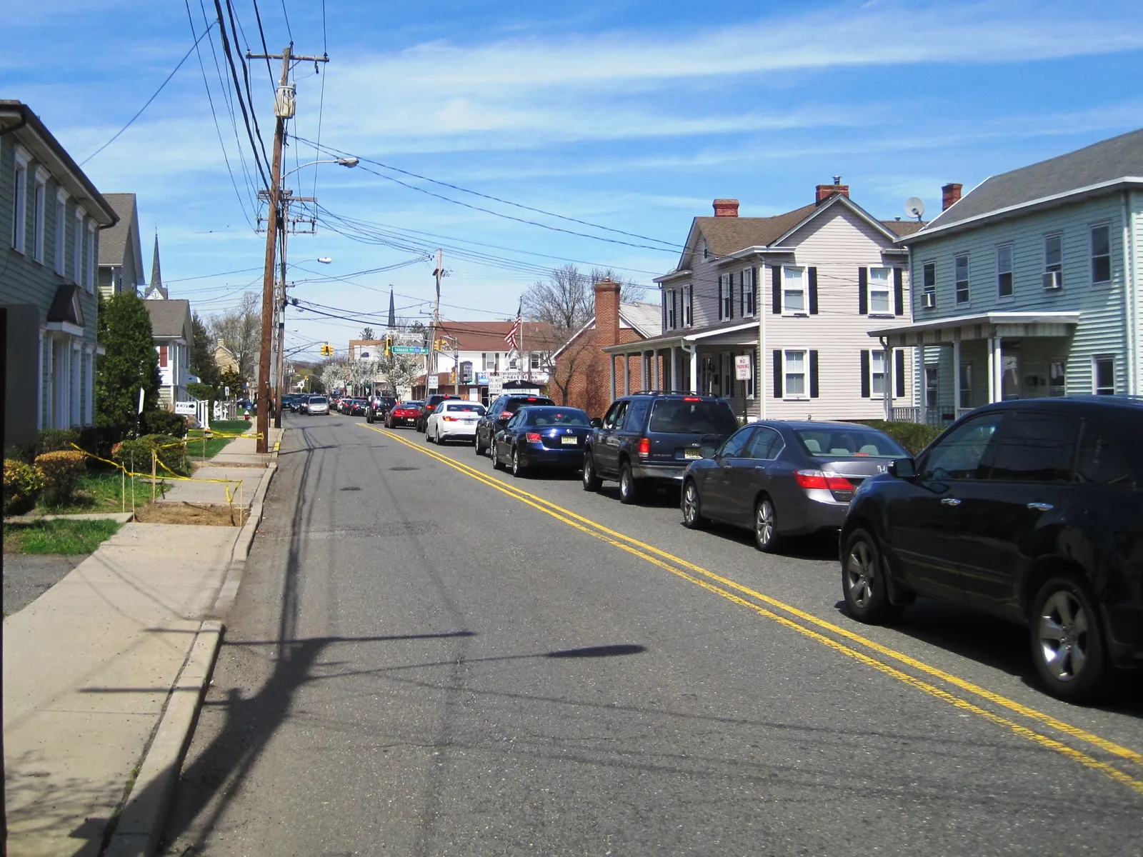A sunny view up Main Street lined with two-story clapboard homes, a church steeple and an American flag in the distance