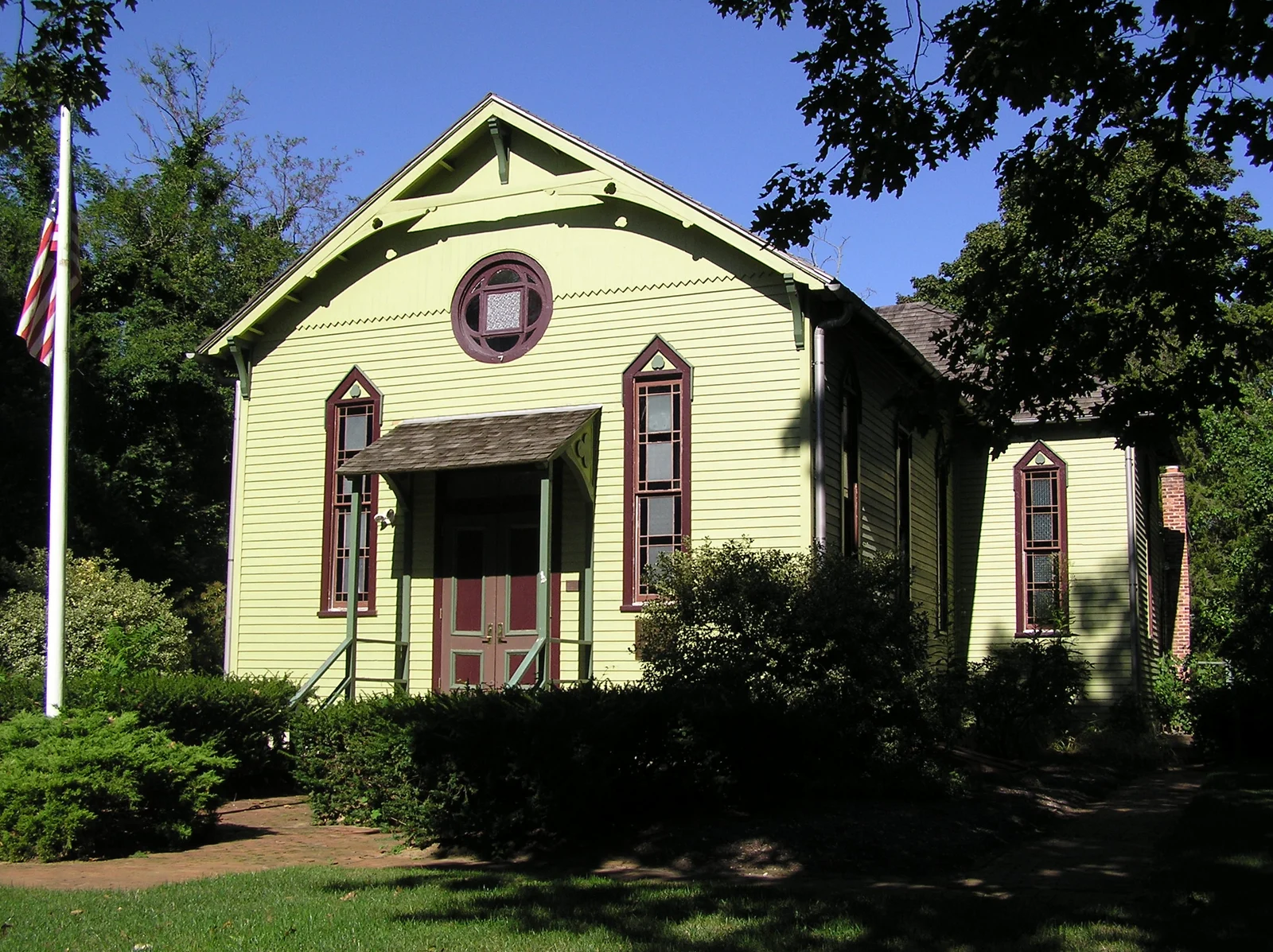 The small pale green 1882 Fisk Chapel with a round window, pointed-arch windows and a red door among shade trees