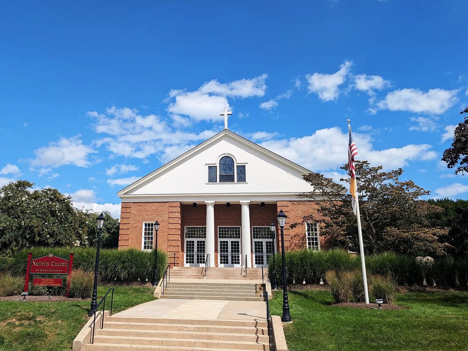 Brick church with white columns and a pediment under a blue sky with puffy clouds