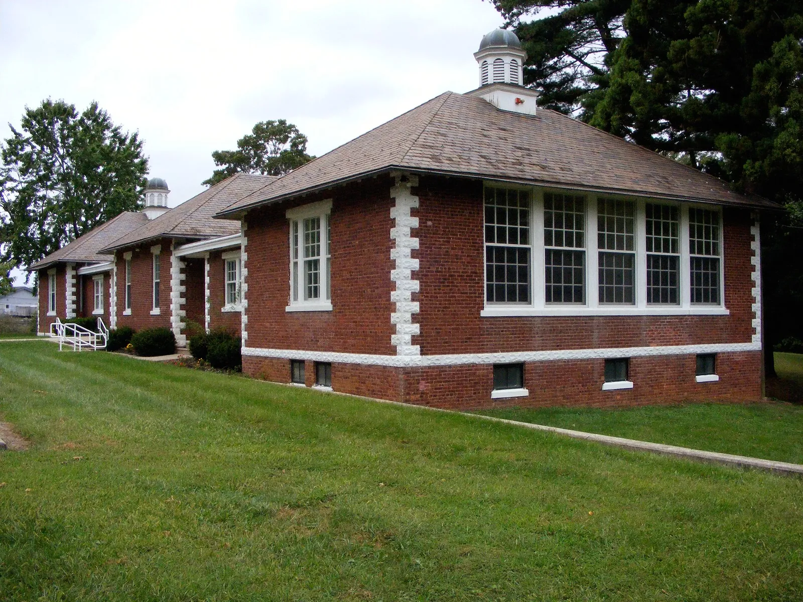 Red brick schoolhouse with white trim and a cupola on a green lawn