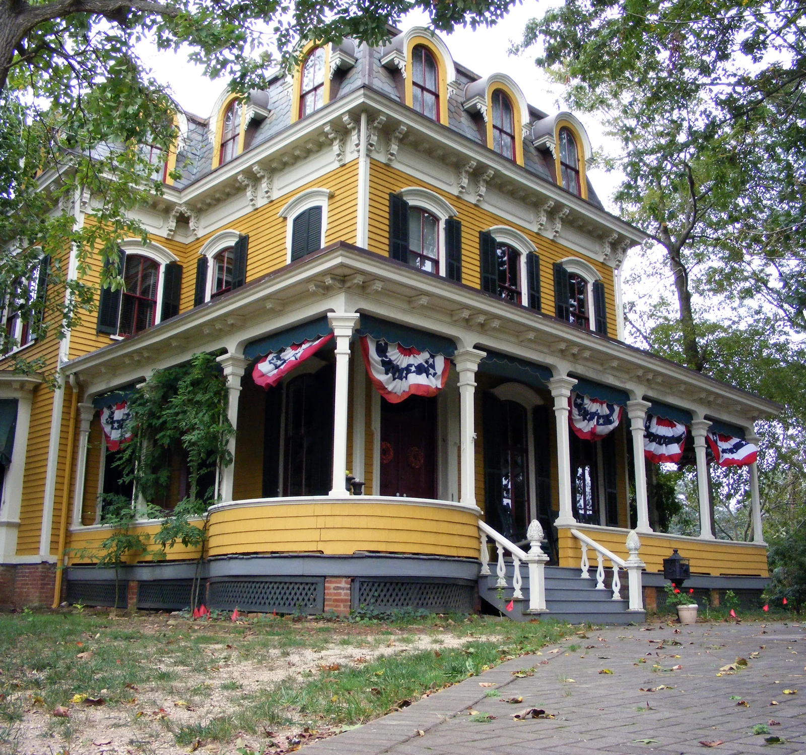 The yellow Second Empire style George Taylor House with a wraparound porch hung with patriotic bunting