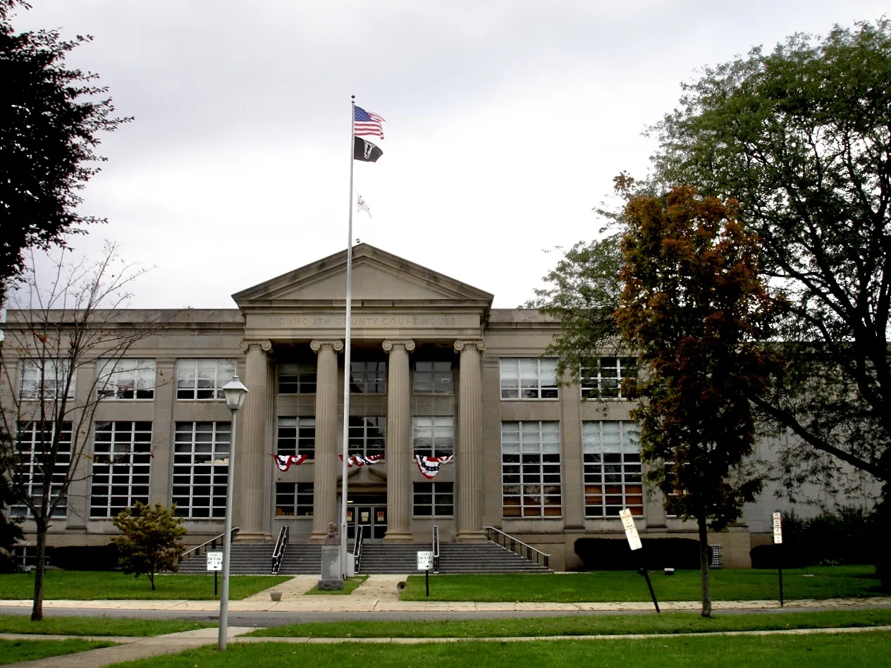 The columned front of the Monmouth County Court House with flags, set back behind a lawn