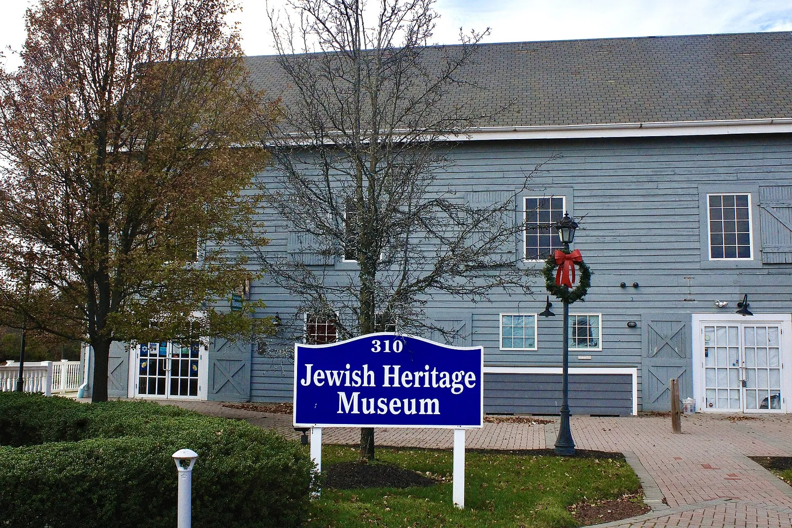 A large blue-gray clapboard barn-style building with white trim, a lamppost with a holiday wreath and a blue museum sign