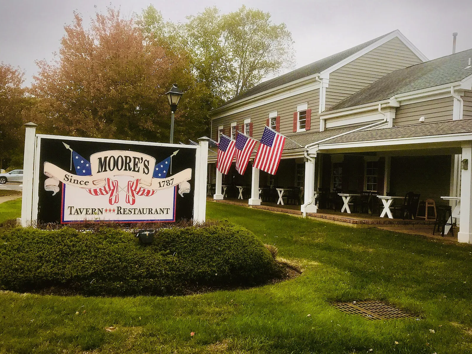 Moore's Tavern sign on a lawn in front of the tavern, with American flags on the porch