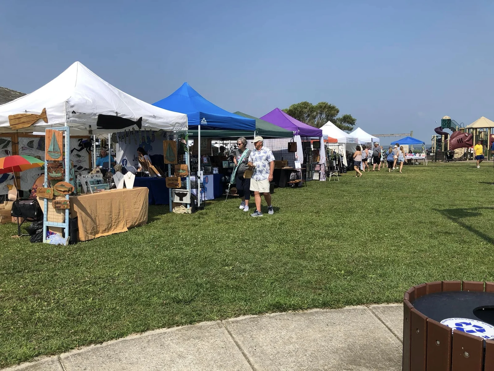 A row of colorful vendor tents with wooden signs and crafts on the grass at a Sunset Park craft show