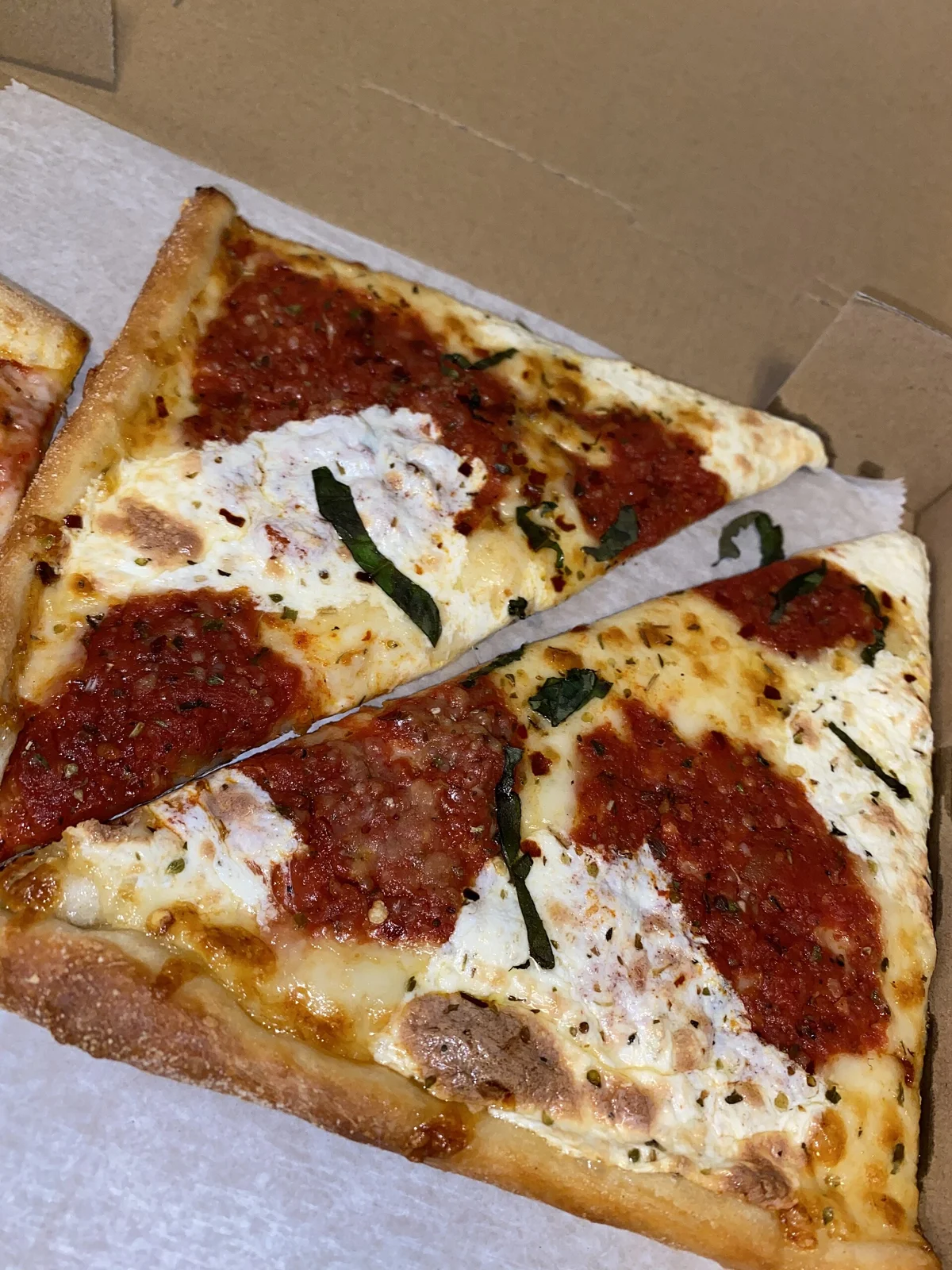 Two square grandma pizza slices with tomato sauce, mozzarella and basil in a box