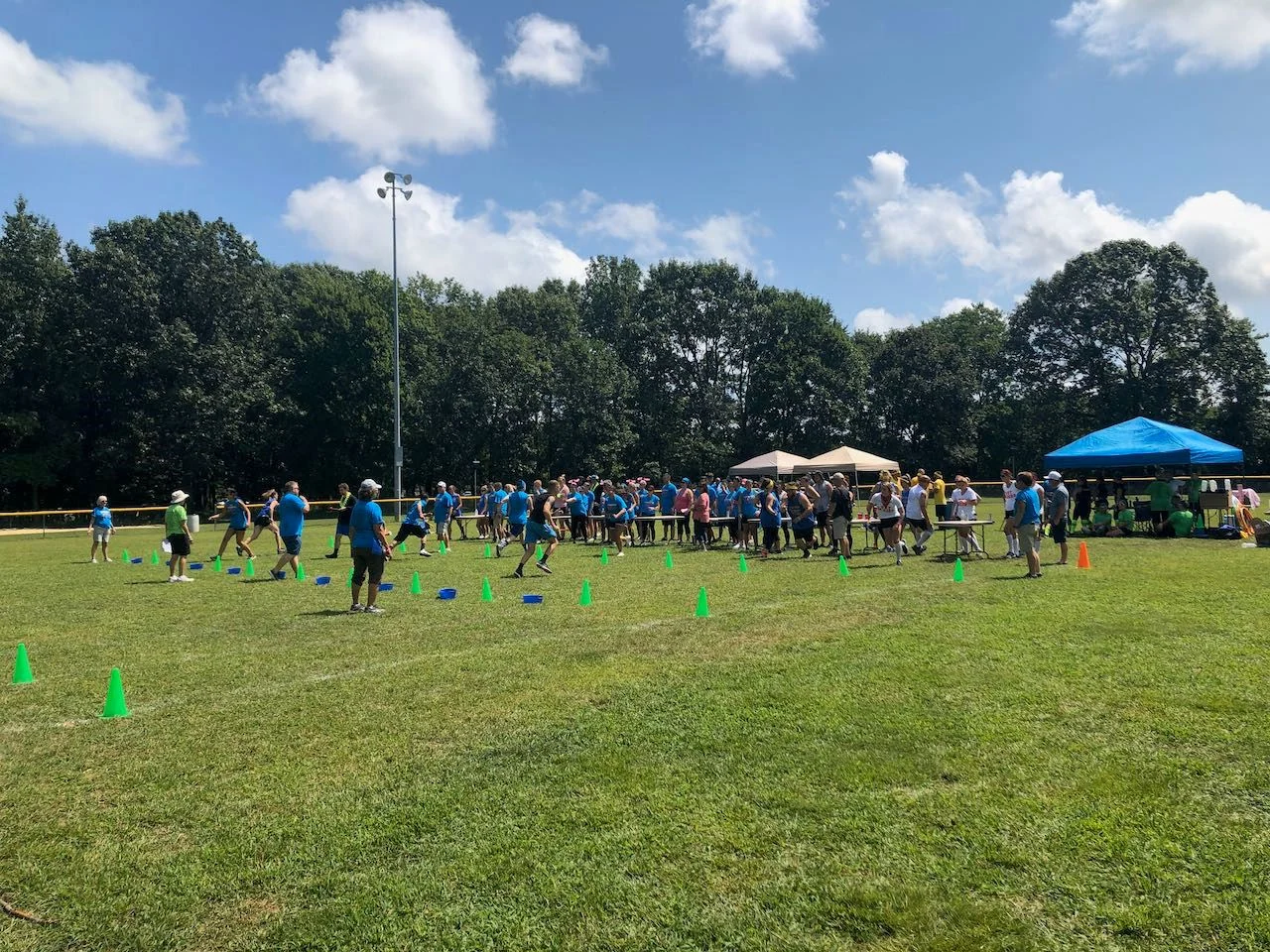 A large group playing field games on the grass at Veterans Park, with canopy tents along the tree line