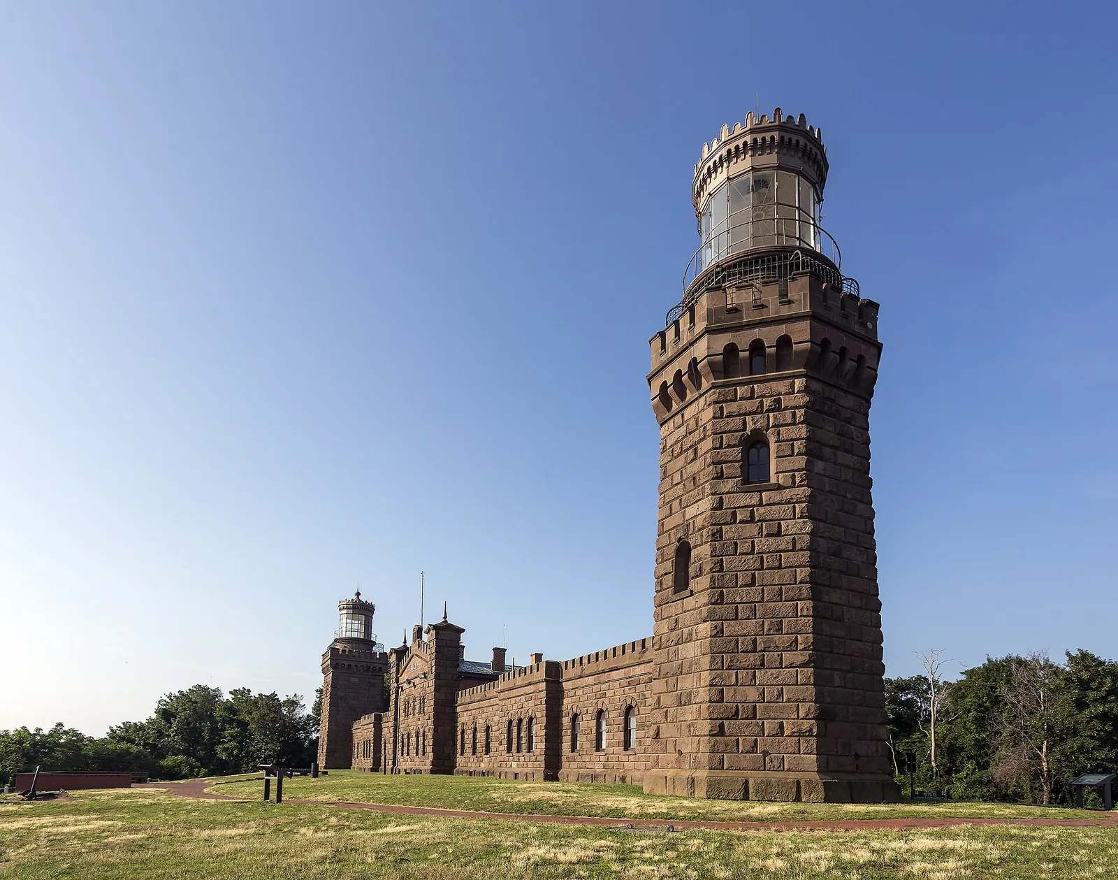 The brownstone Navesink Twin Lights, a castle-like lighthouse with two towers, on a grassy bluff under a blue sky