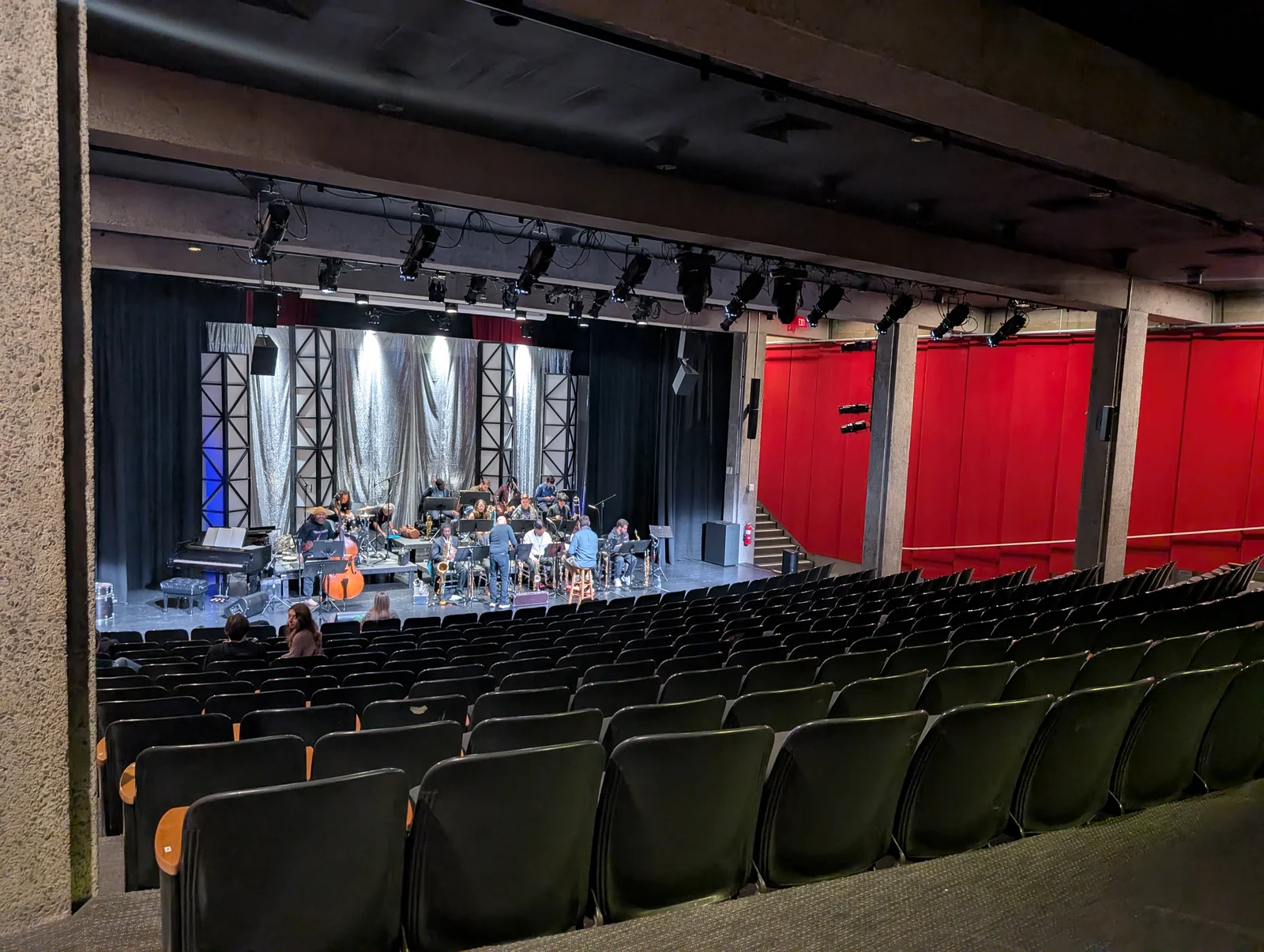 A band rehearsing on the stage of the Bell Theater, seen from rows of seats, with red curtains to the side