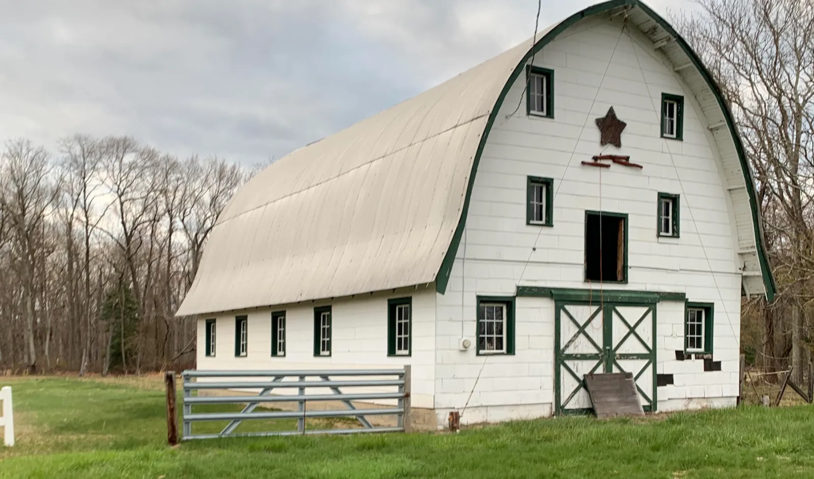White gambrel-roof barn with a star above the doors, set against bare trees