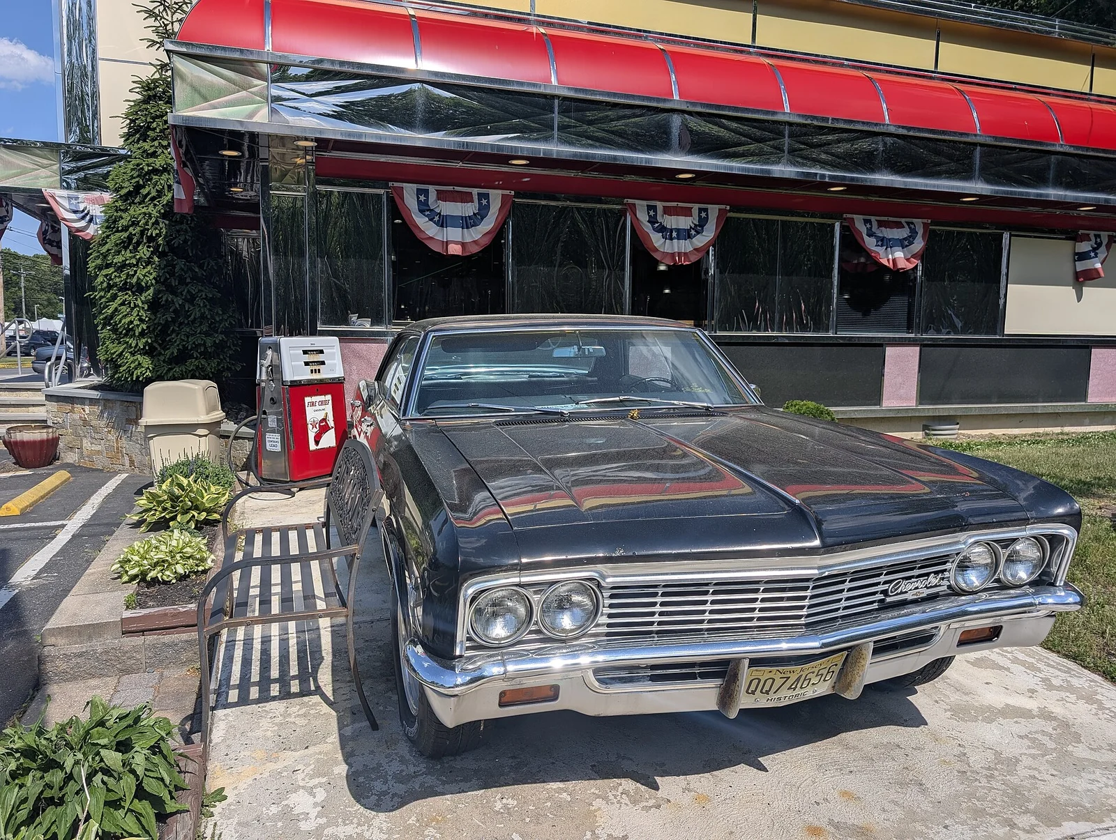 A black 1960s Chevrolet parked beside a vintage gas pump outside JB's Diner