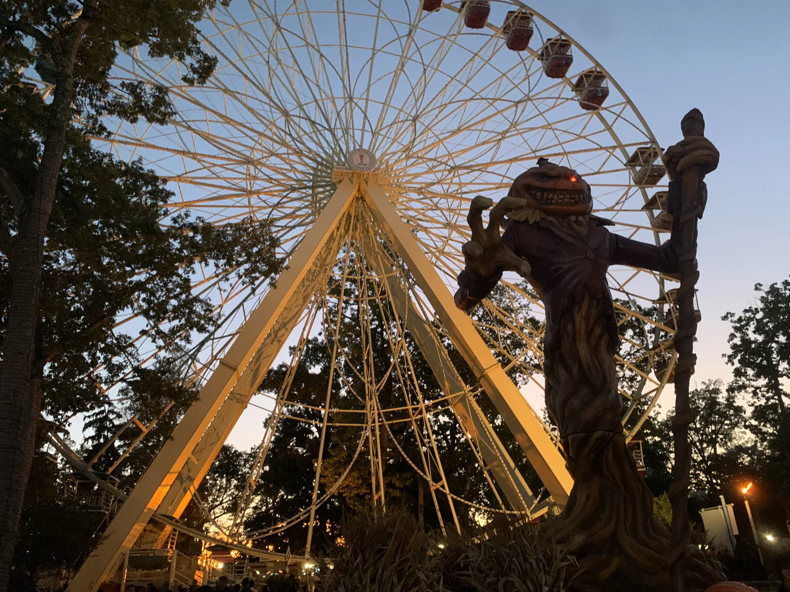 A tall Fright Fest figure beside the lit Ferris wheel at dusk at Six Flags Great Adventure