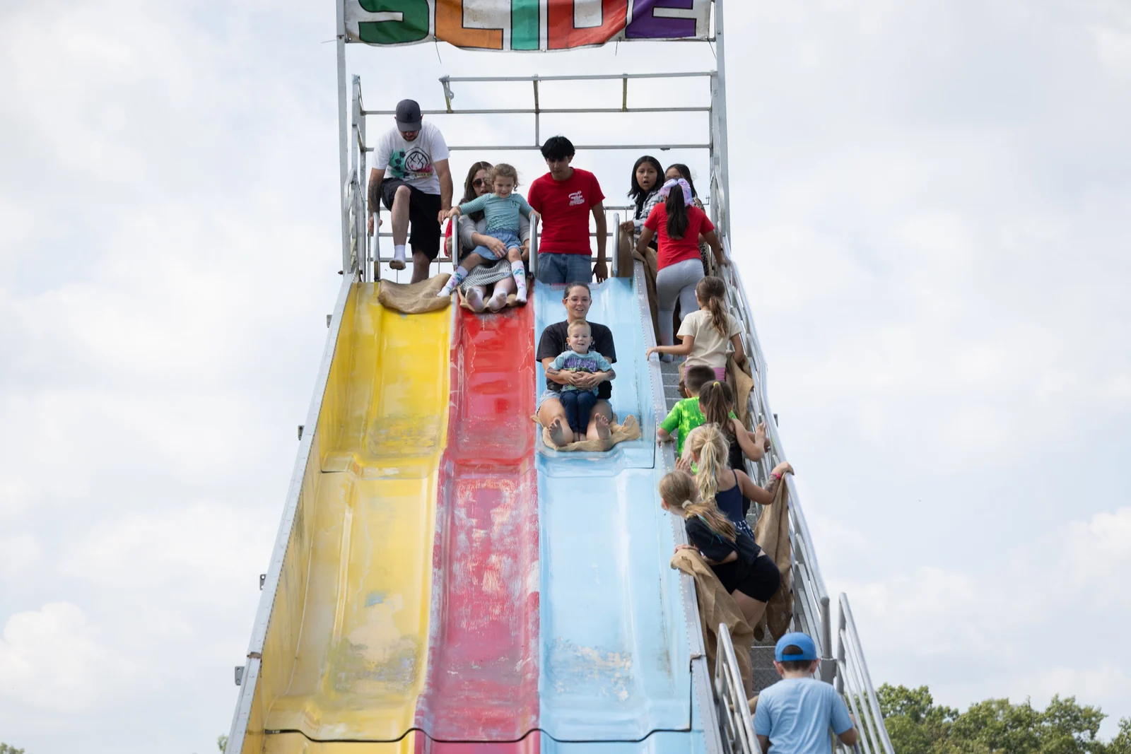 Riders racing down a tall yellow, red and blue inflatable Fun Slide at Jackson Day