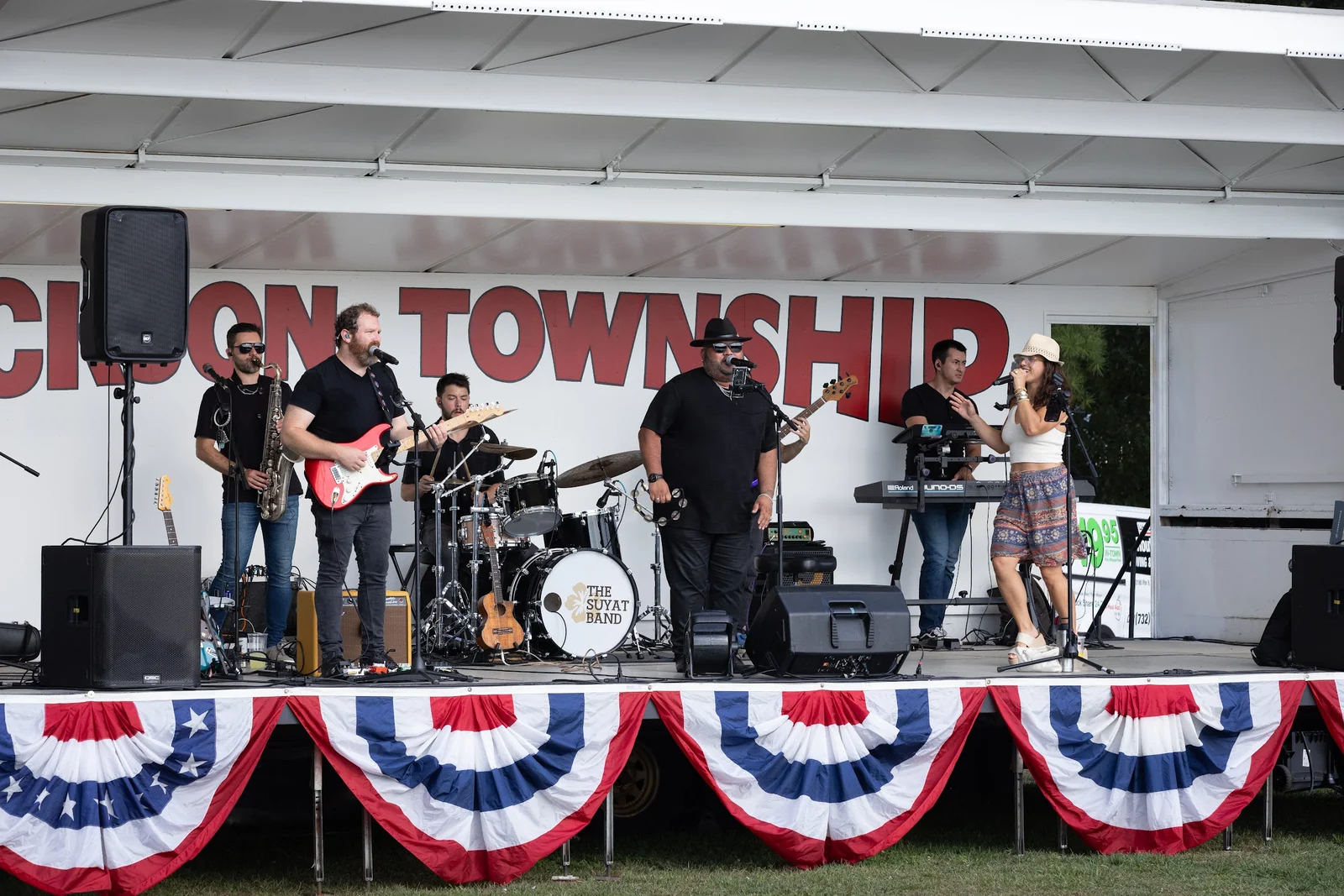 A band with guitars, keyboard and drums playing on the red, white and blue Jackson Township stage