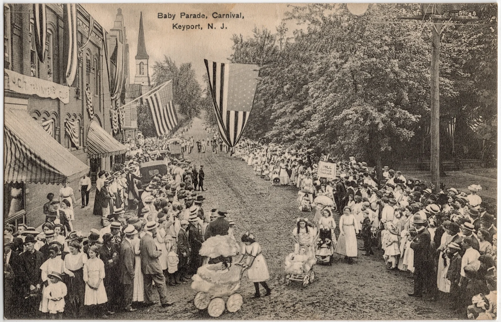 Early 1900s postcard of a crowded, flag-draped Keyport street during the Baby Parade, with decorated baby carriages