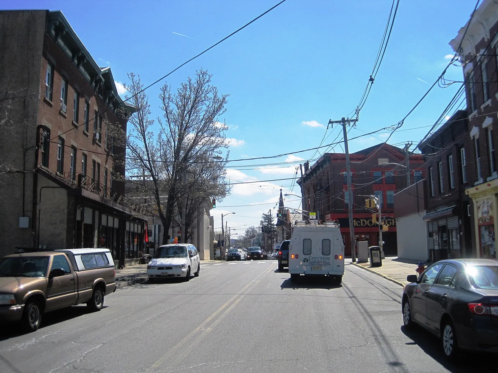 A downtown street lined with tall nineteenth-century brick buildings under a blue sky