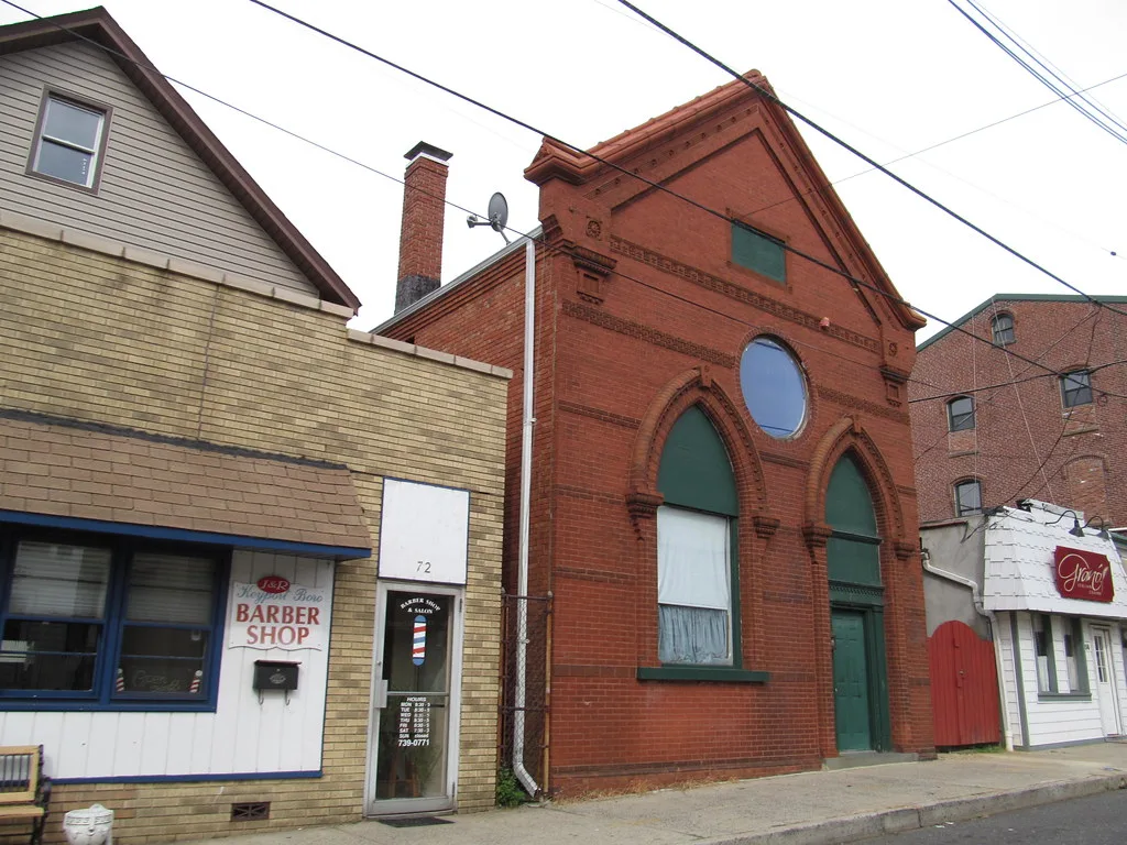A red brick building with arched windows and a round window beside smaller storefronts in Keyport
