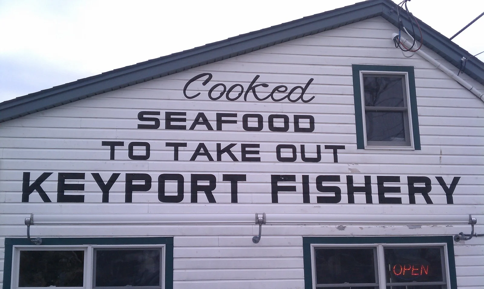 White clapboard building with a sign reading Cooked Seafood to Take Out, Keyport Fishery