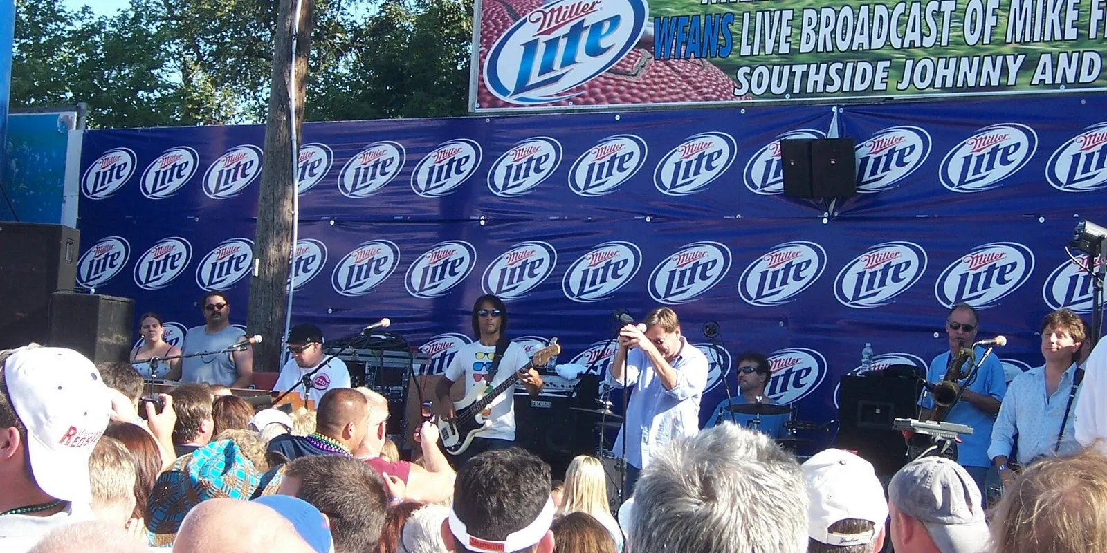 A band playing on an outdoor stage to a packed crowd