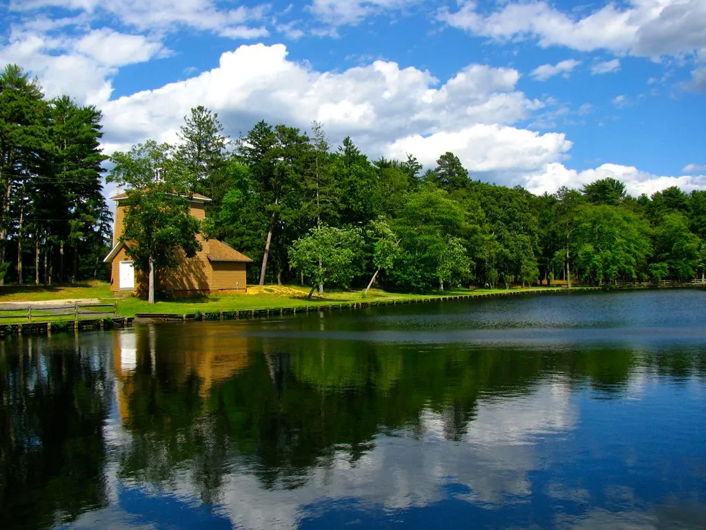 Lake in Ocean County Park with a building among the trees and clouds reflected in the water