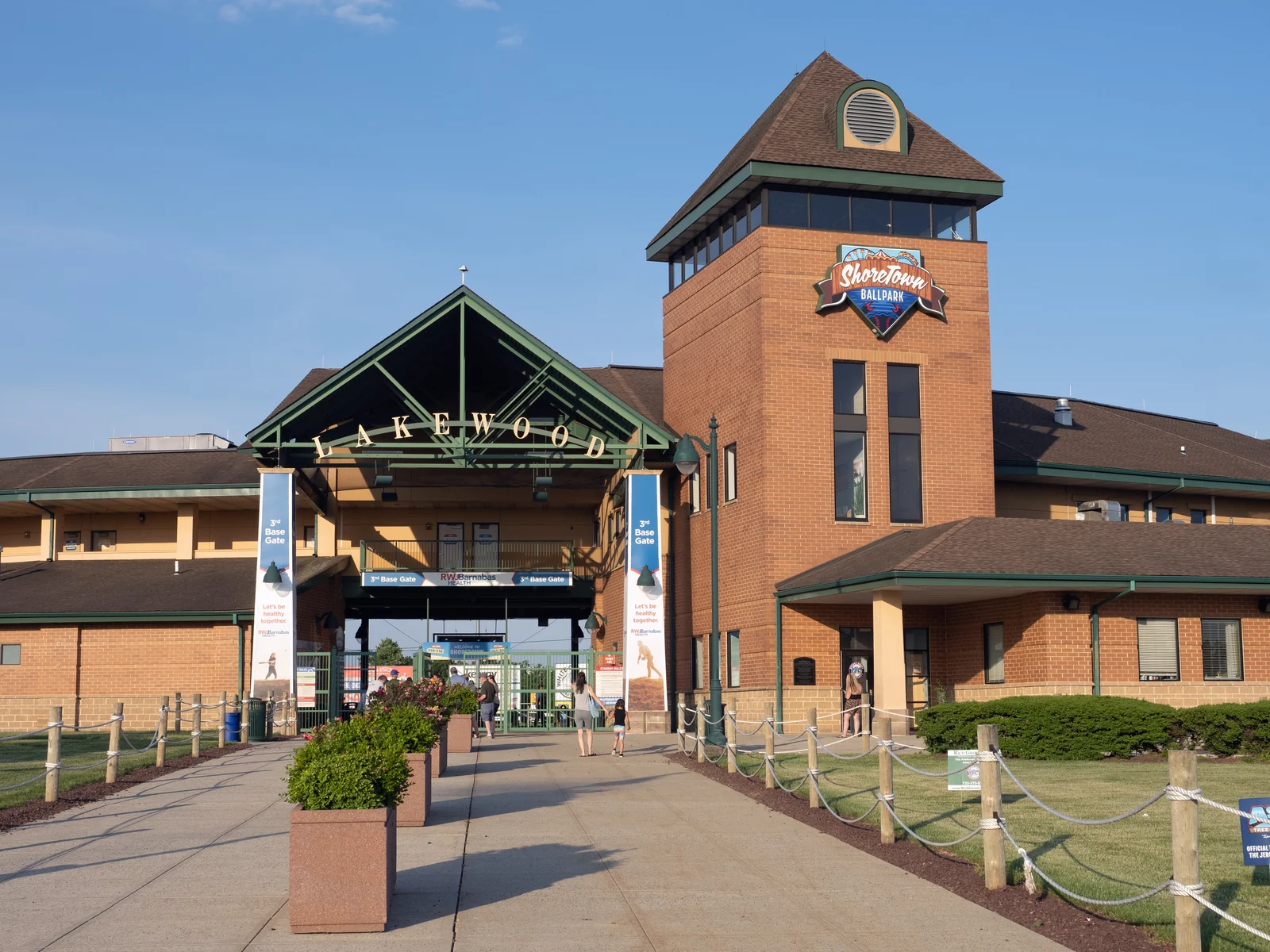 Brick tower with the ShoreTown Ballpark logo beside the gabled Lakewood entrance gate under a blue sky