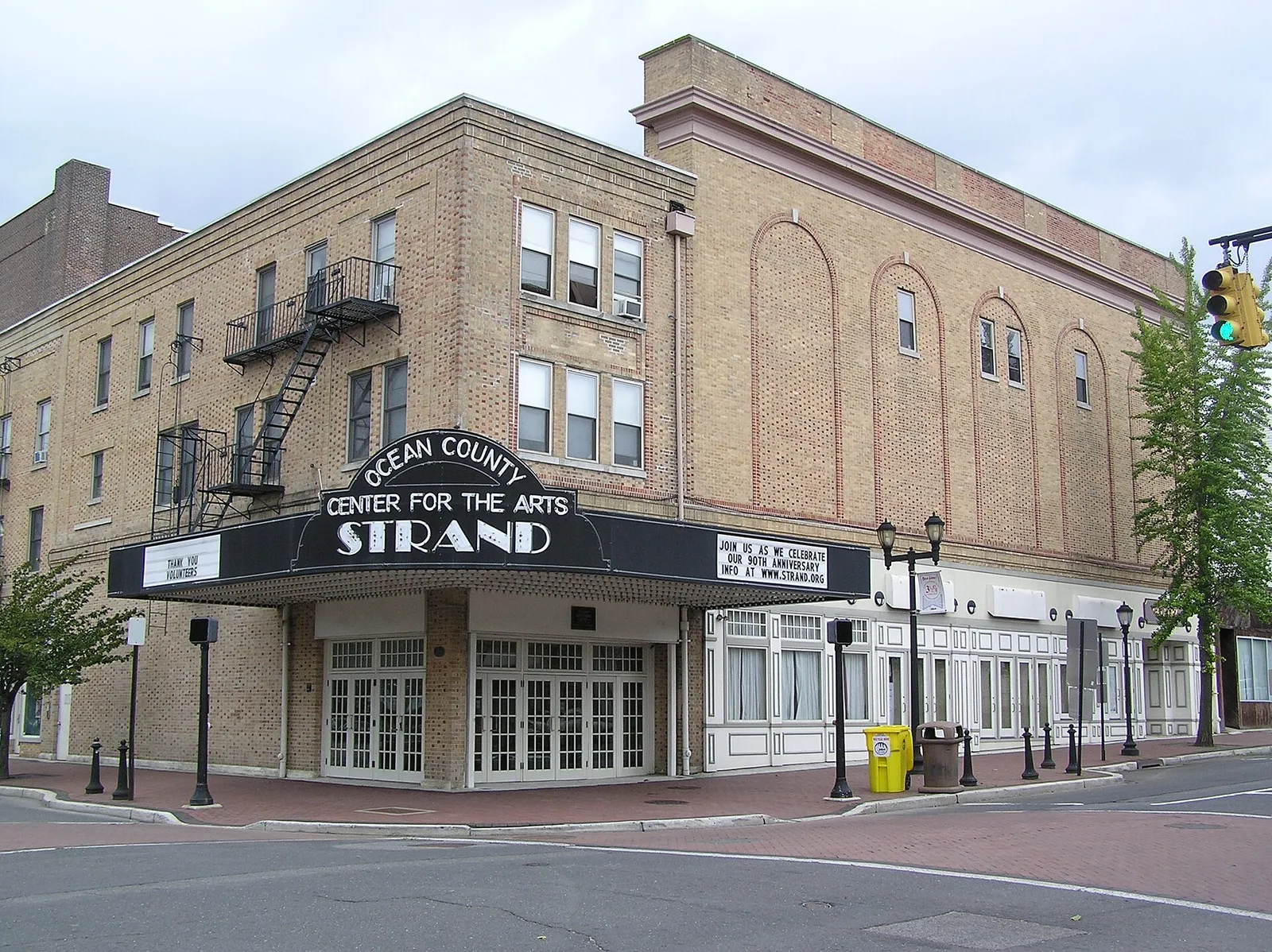 A tan brick theater building with a black marquee reading Strand on a downtown corner