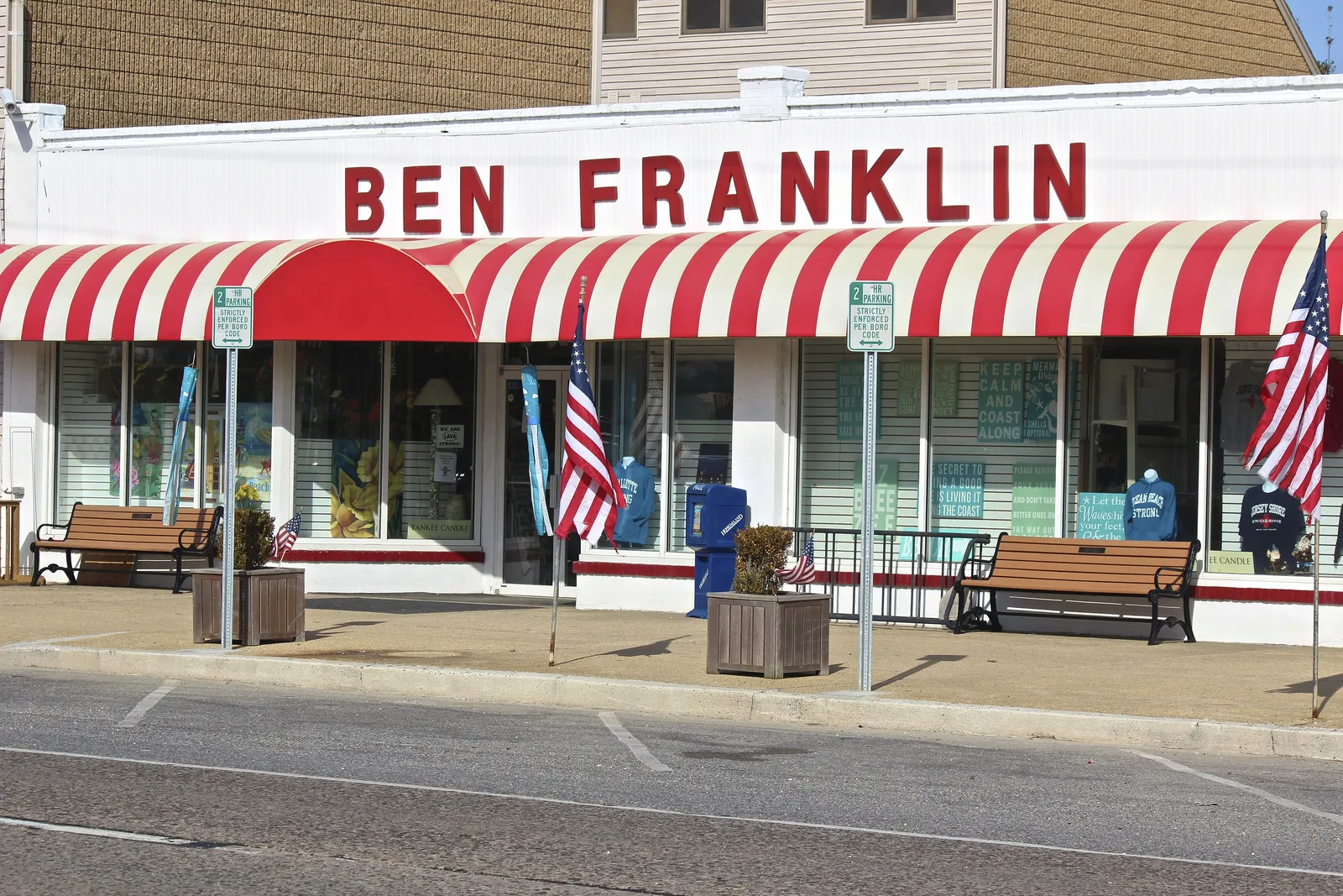 A shop front with a red and white striped awning, flags and benches out front