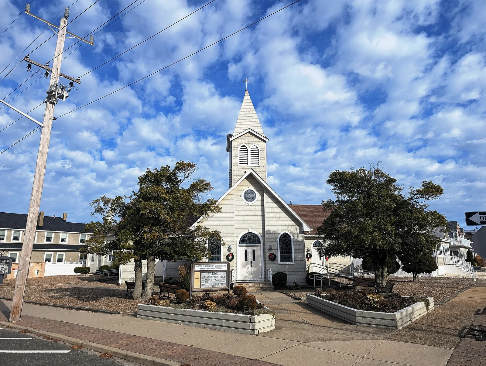 White clapboard Union Church of Lavallette with a tall steeple, framed by two trees, under a blue sky with puffy clouds