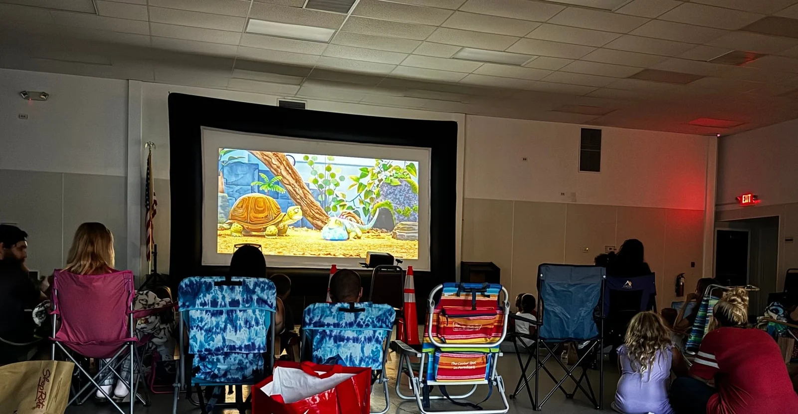 An audience in folding chairs watches an animated film on a big inflatable screen at the township's End of Summer Movie Night
