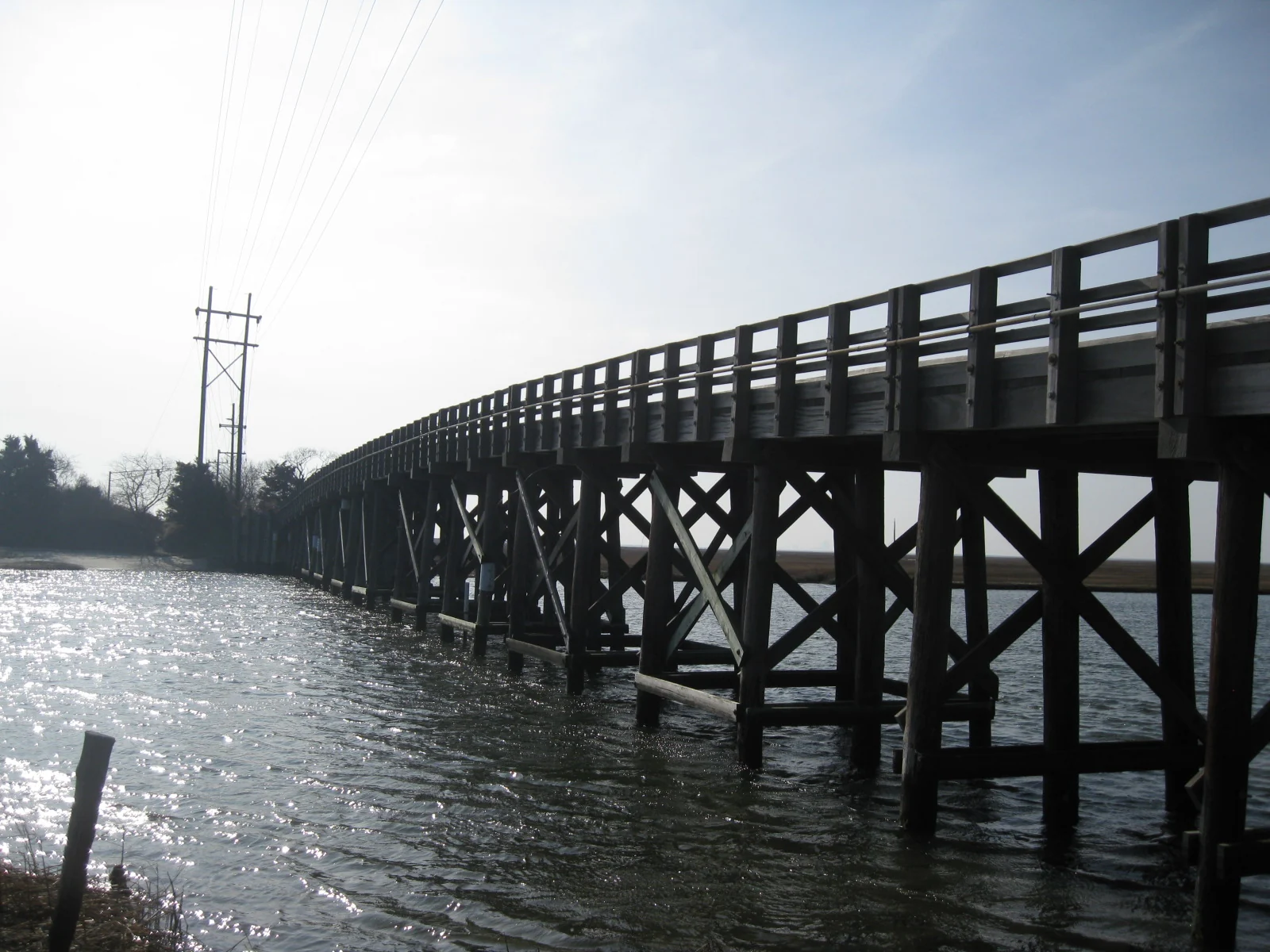 Wooden trestle bridge carrying Great Bay Boulevard over a tidal creek, with sunlight glinting on the water