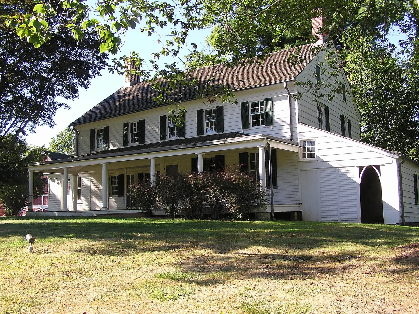 The white Parker Homestead farmhouse with a long front porch and green lawn under tall trees in Little Silver