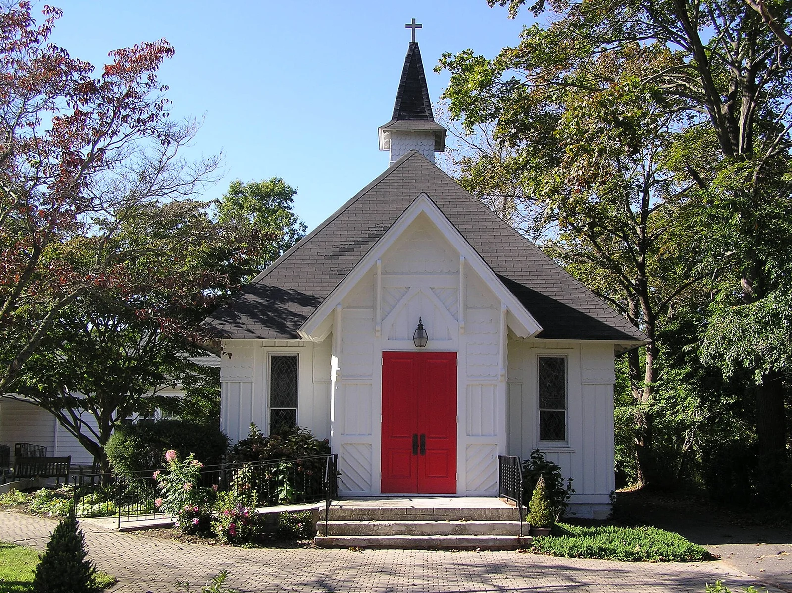 Small white Gothic-style St. John's Episcopal Church with a steeple and bright red front doors among shade trees