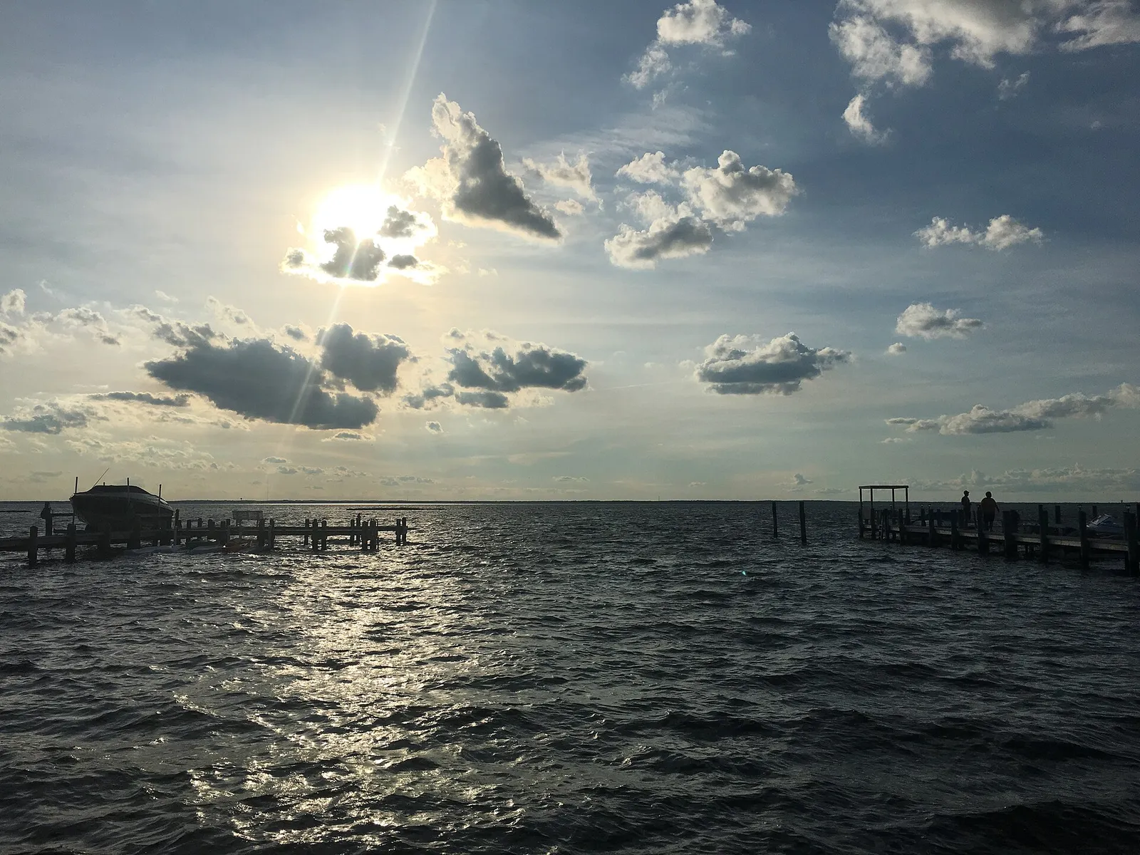 Sun shining through clouds over choppy bay water with wooden docks and pilings