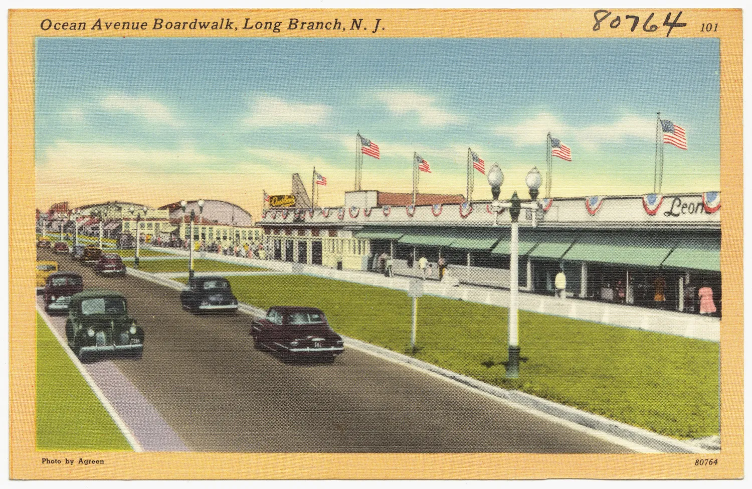 Vintage color postcard of the Ocean Avenue boardwalk with flags and old cars