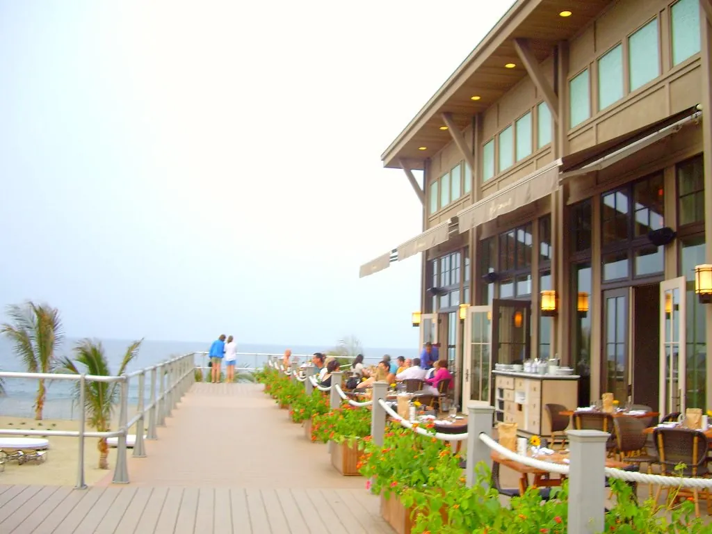 Restaurant patio with tables and planters along the boardwalk at Pier Village, palm trees and the ocean beyond