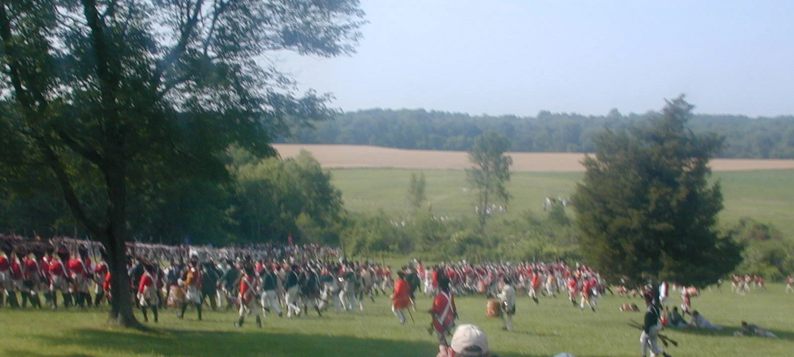 Lines of reenactors in red British coats and Continental uniforms moving across a field during the Battle of Monmouth reenactment