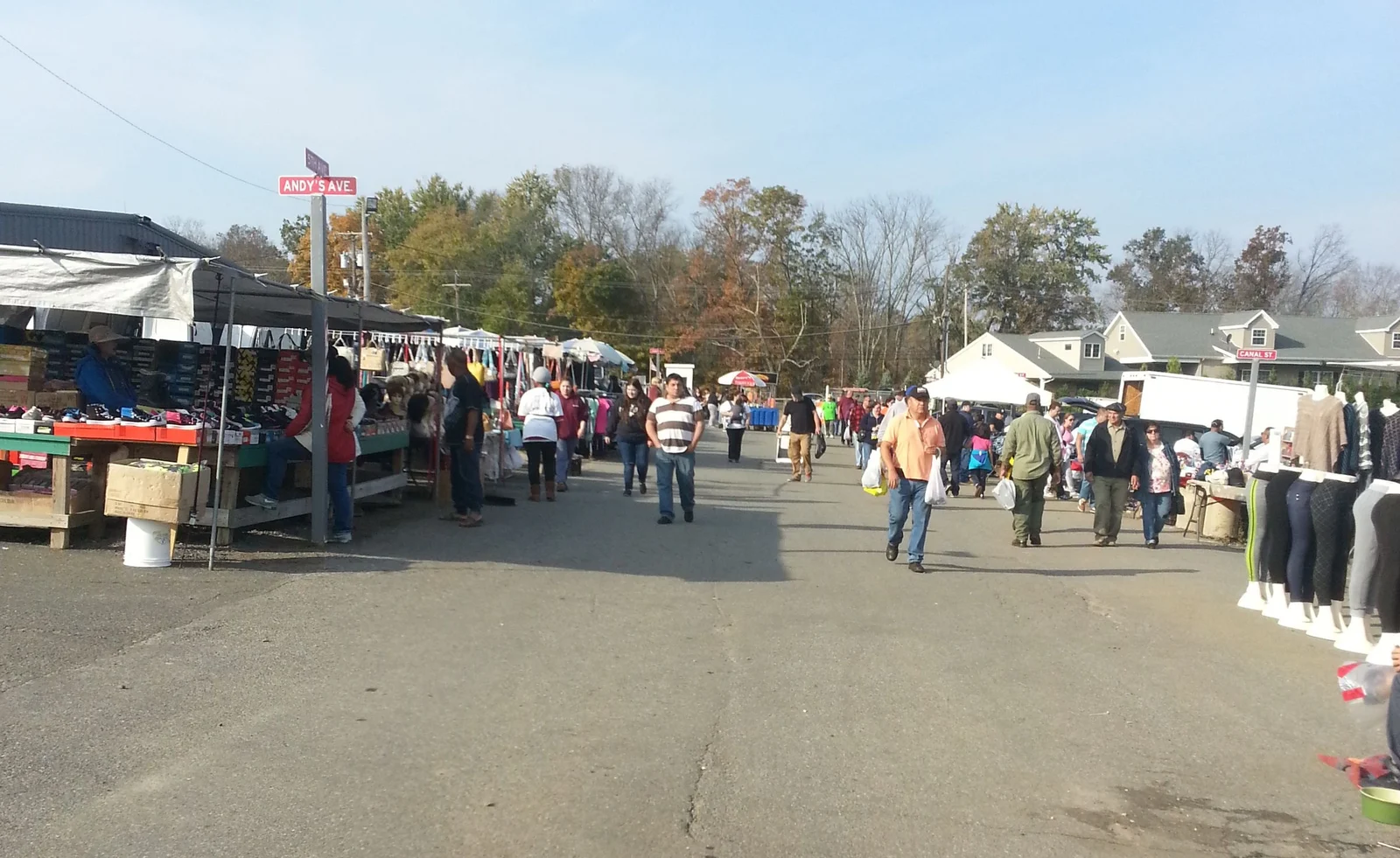 Shoppers walking down a long aisle of vendor stalls and clothing racks at the Englishtown Auction on an autumn morning