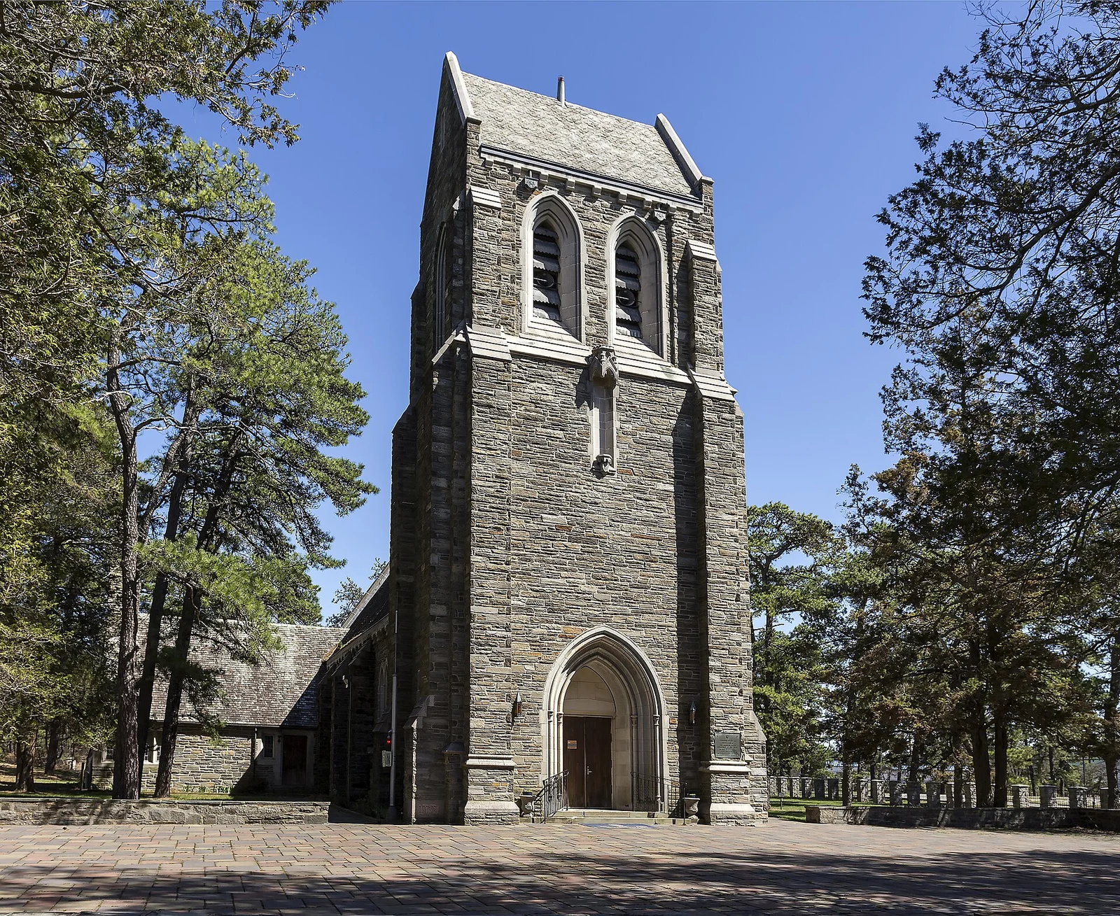 Gothic stone bell tower and arched doorway of the Cathedral of the Air framed by pitch pines under a blue sky