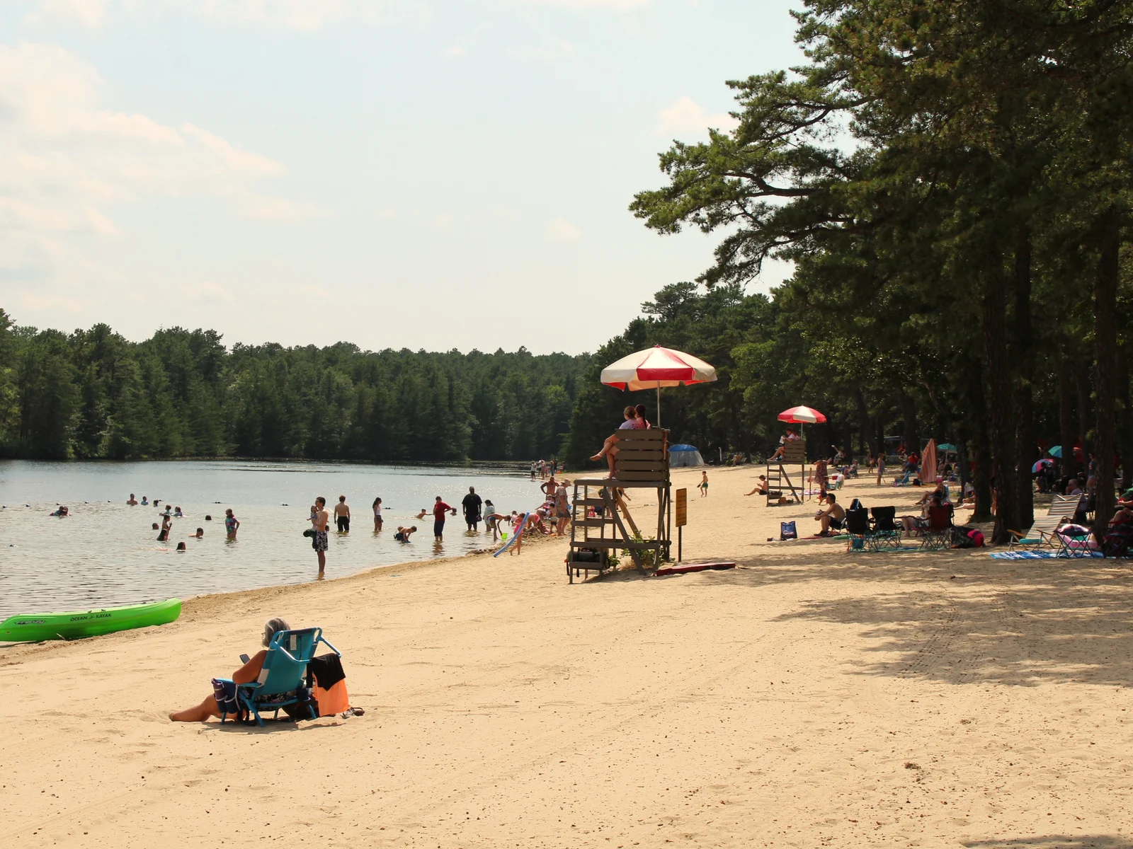 The sandy swimming beach at Harry Wright Lake, with a lifeguard stand, umbrellas and pine woods across the water