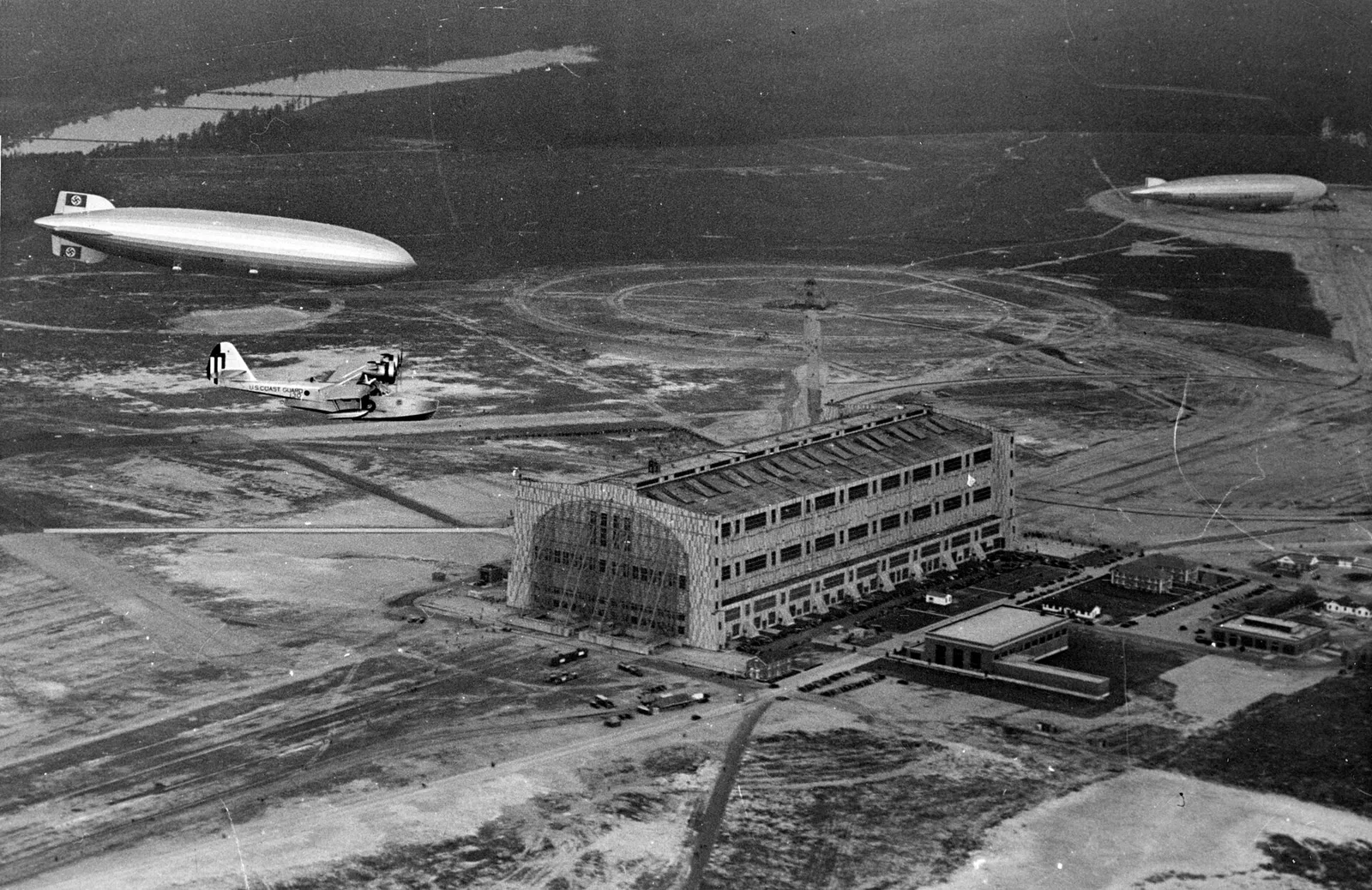 Black and white 1936 photo of the airship Hindenburg flying over the Lakehurst air station