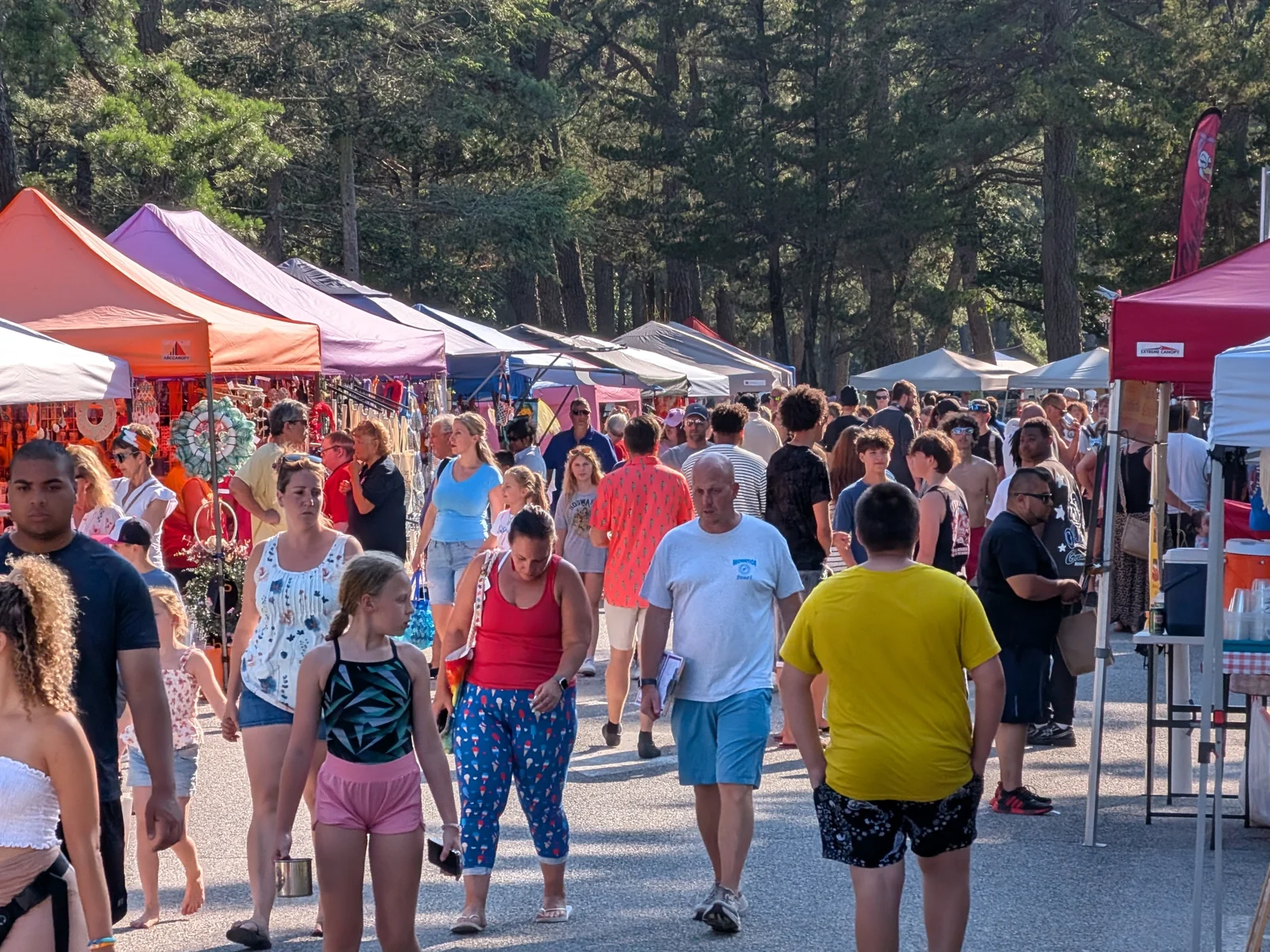 Crowds stroll a row of vendor tents under the pines at Manchester Day